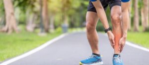 Person running outdoors on path and bending over holding shin in pain