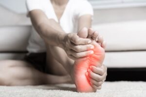 Person sitting on floor cross-legged and rubbing foot in pain