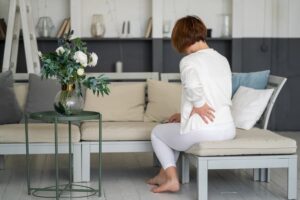 Person sitting at home on couch holding side of lower back in pain